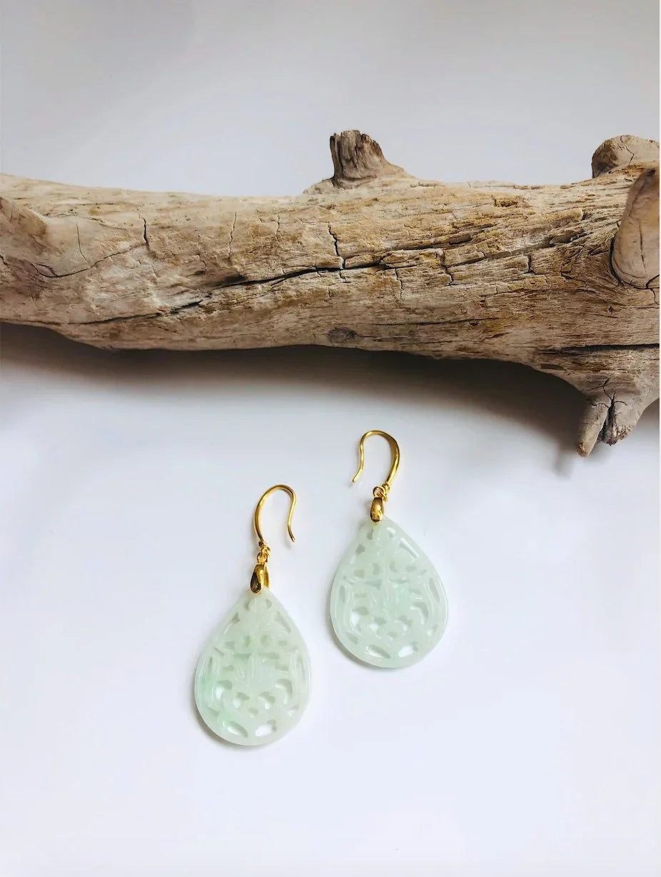 Teardrop-shaped lace earrings with gold hooks on a white background with a piece of driftwood.