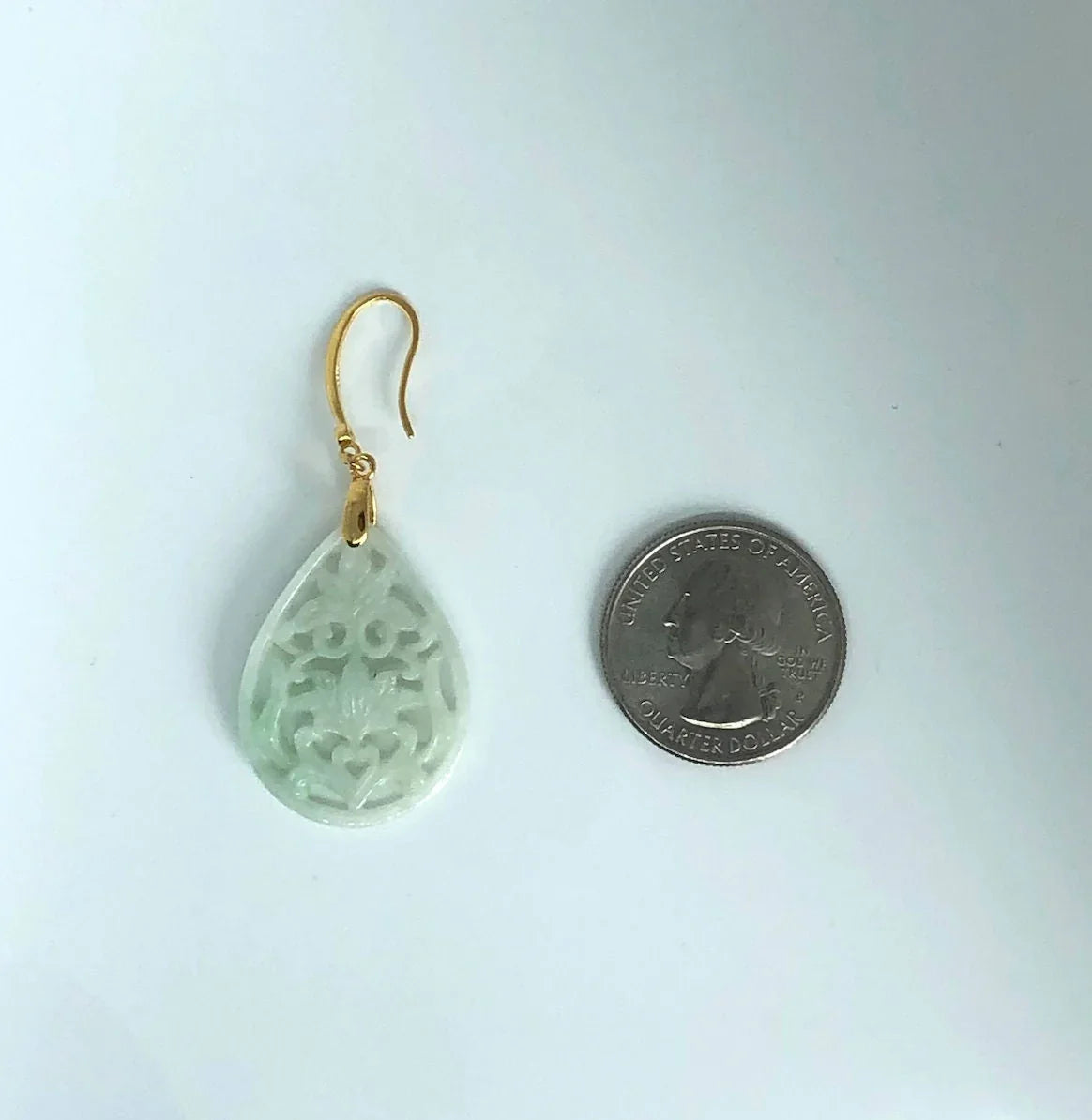 Green teardrop earring with gold hook on a white background, next to a quarter for scale.