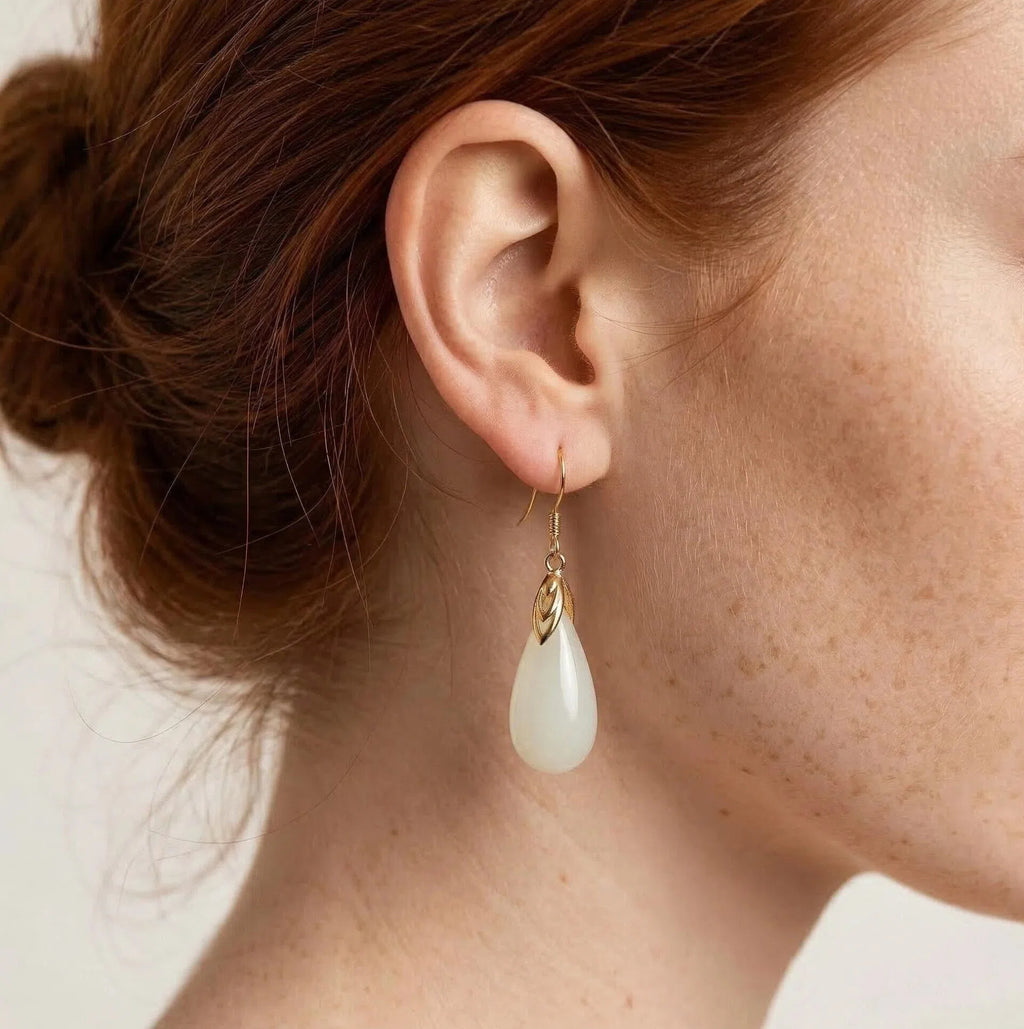 Close-up of an ear wearing a gold earring with a white teardrop pendant.