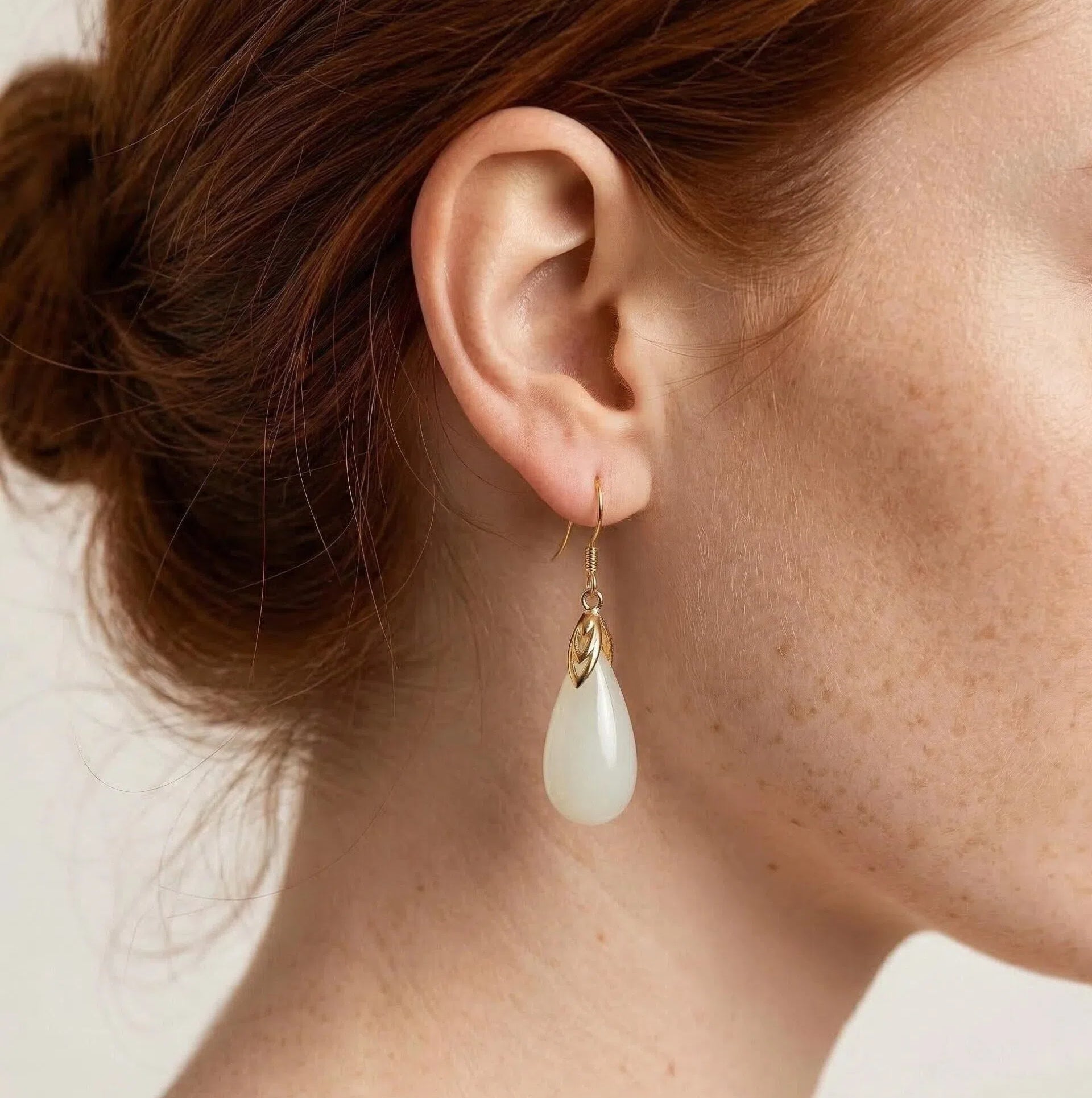 Close-up of an ear wearing a gold earring with a white teardrop pendant.